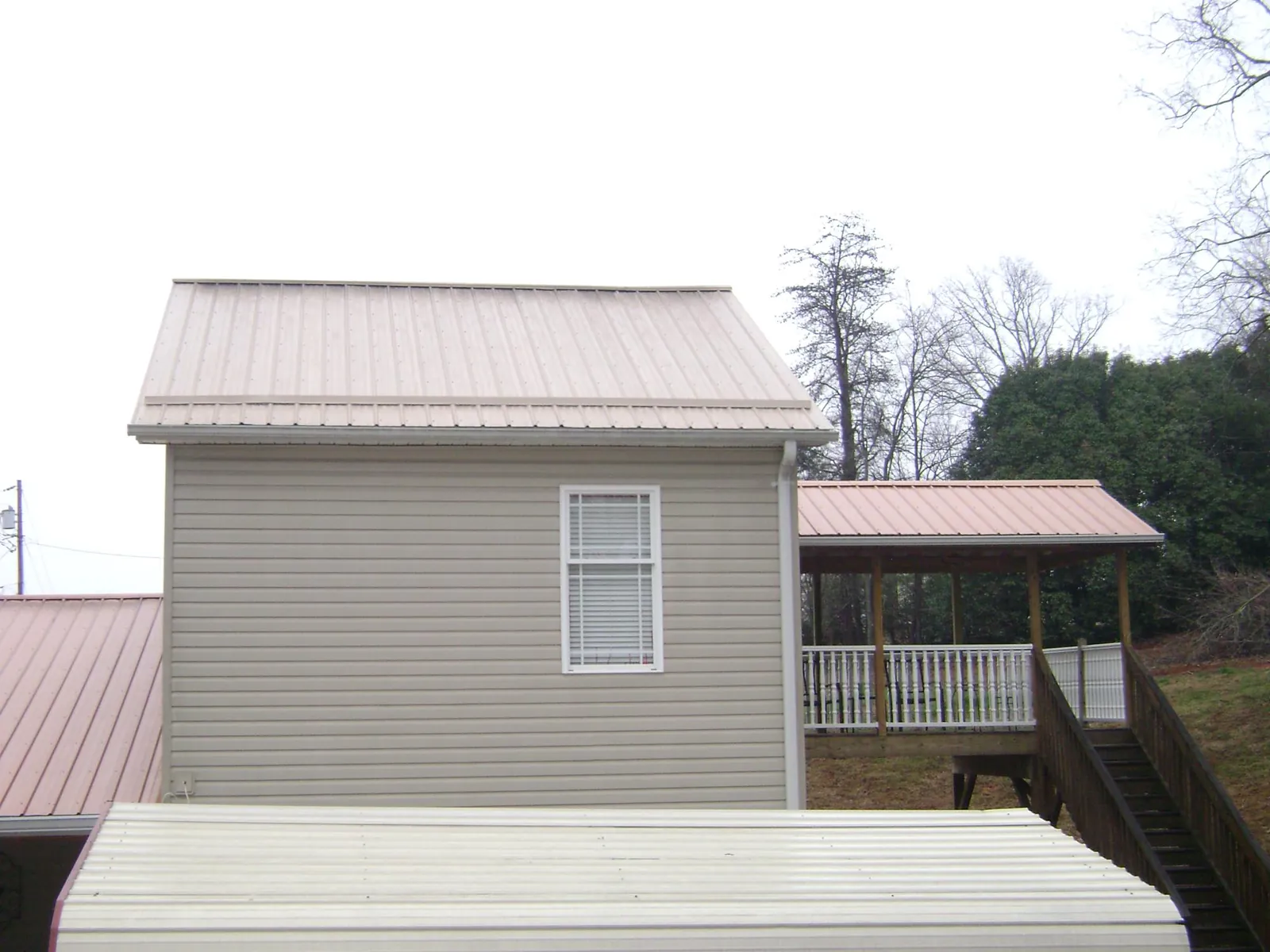 Tan metal roofs on a two story addition and attached porch, from a Roof Replacement job in Rogersville